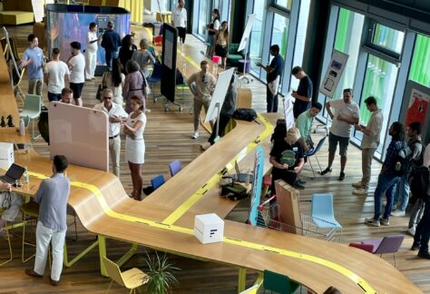 In einem Konferenzsaal werden um verschiedene Plakate Gespräche zum Thema Co-Founding geführt