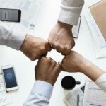 Vier Menschen schlagen die Fäuste aneinander um ein Buisness Erfolg zu feiern.