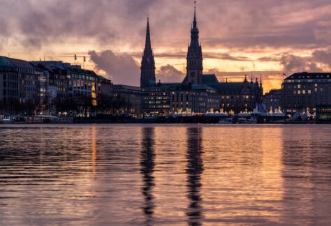 Das Hamburger Rathaus im Sonnenaufgang mit der Alster vor sich.