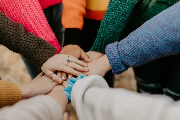 Symbolic image for teamwork, several arms in a circle, placing their hands on top of each other in the middle, workshop, photo Hannah Busing, Unspleash